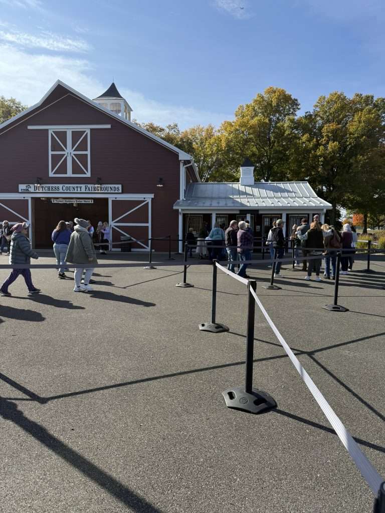 Knitters gathering at the Dutchess County Fairgrounds red barn entrance at Rhinebeck Sheep and Wool Festival with fall foliage in background