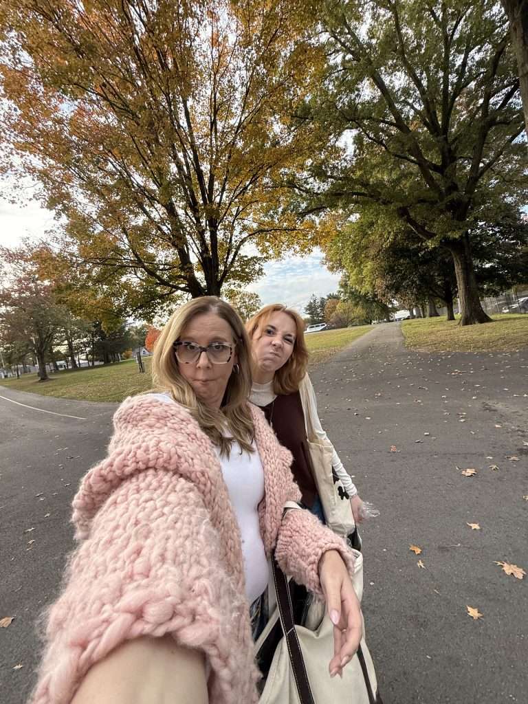 Woman wearing hand-knit pink cardigan sweater with daughter on tree-lined path at Rhinebeck with fall leaves on ground