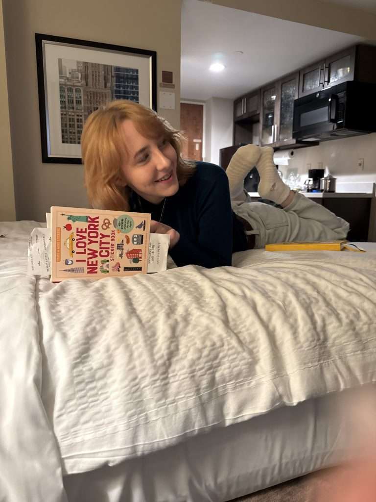 Woman holding "I Love New York City" guidebook in hotel room bed with Manhattan skyline art on wall